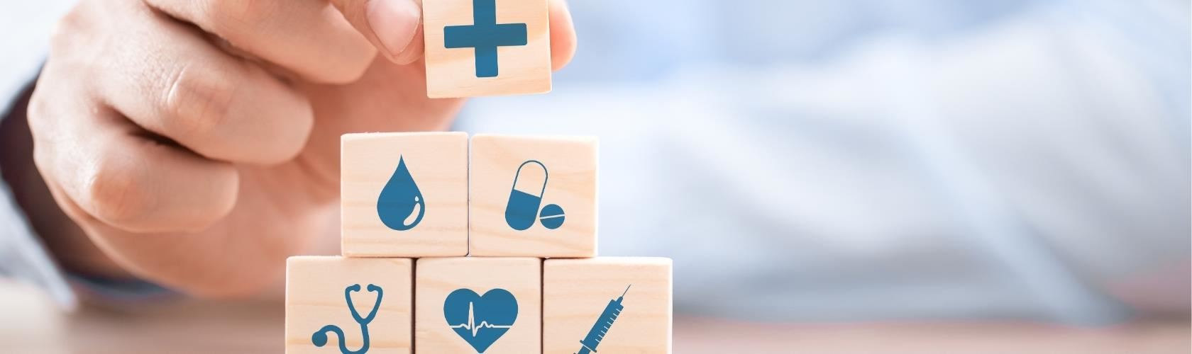 person stacking wooden blocks with medical symbols like a red cross, stethoscope, heart, syringe